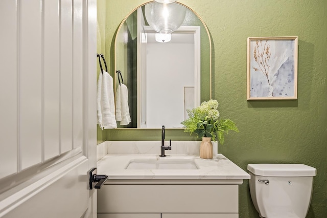 bathroom featuring toilet, vanity, and a textured wall