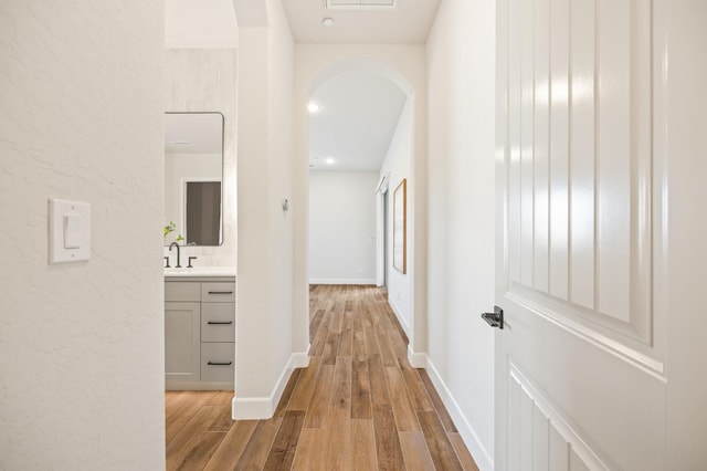corridor with arched walkways, a sink, baseboards, and wood finished floors