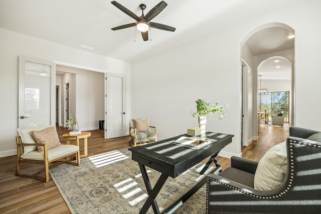office space featuring baseboards, arched walkways, light wood-style floors, and ceiling fan