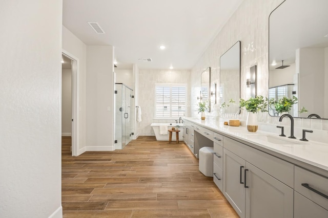 bathroom featuring visible vents, wood finished floors, a stall shower, a freestanding tub, and vanity