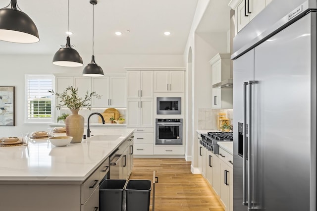 kitchen featuring light wood-type flooring, a sink, white cabinetry, appliances with stainless steel finishes, and decorative backsplash