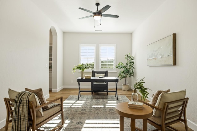 office space featuring arched walkways, baseboards, light wood-style floors, and a ceiling fan