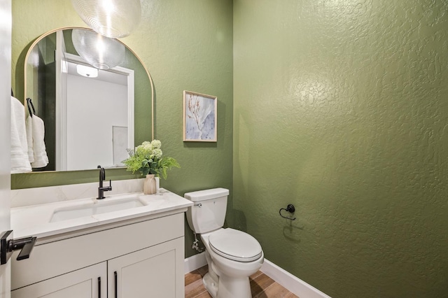 bathroom with vanity, wood finished floors, baseboards, toilet, and a textured wall