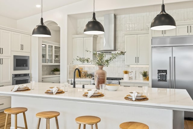 kitchen with a spacious island, backsplash, wall chimney range hood, built in appliances, and a kitchen bar