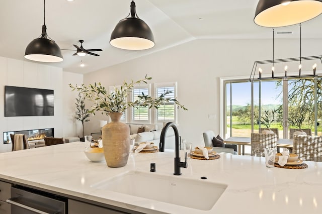 kitchen featuring a tiled fireplace, a sink, open floor plan, light stone countertops, and vaulted ceiling