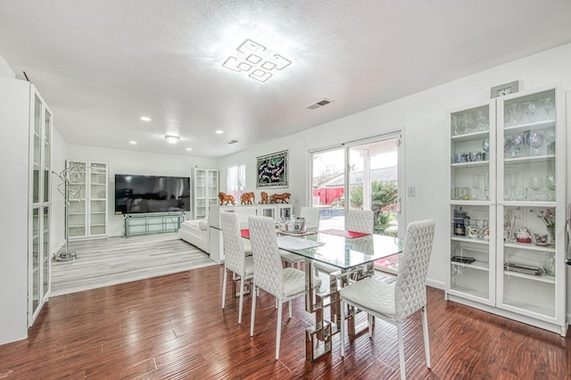dining space with wood finished floors, a textured ceiling, and visible vents
