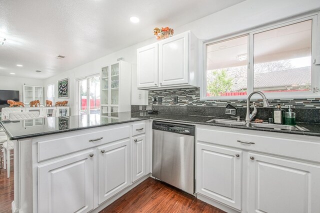 kitchen featuring a peninsula, dark wood-type flooring, stainless steel dishwasher, a sink, and backsplash