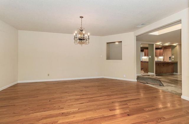 unfurnished dining area with wood finished floors, visible vents, baseboards, and an inviting chandelier