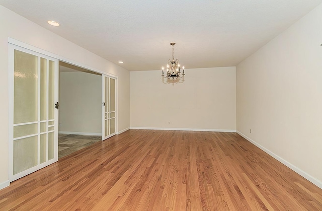 unfurnished room with baseboards, a notable chandelier, and light wood-type flooring