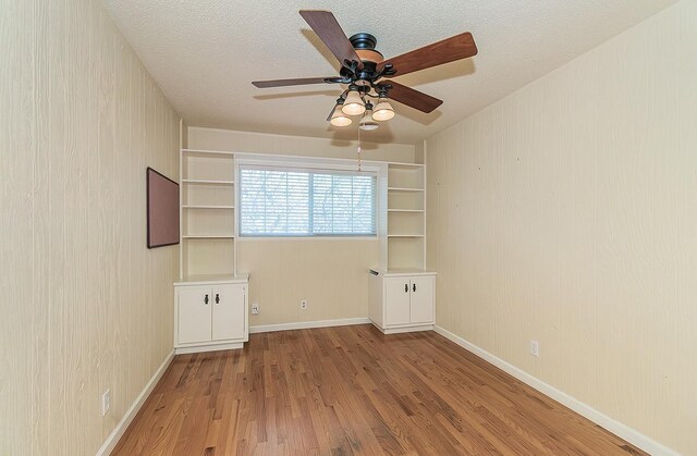 unfurnished room featuring baseboards, wood finished floors, a textured ceiling, and ceiling fan