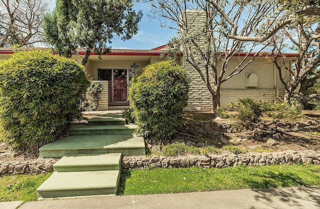 view of property hidden behind natural elements featuring a chimney and stucco siding