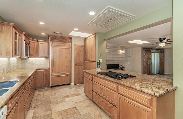 kitchen featuring visible vents, light stone countertops, tasteful backsplash, a brick fireplace, and built in appliances