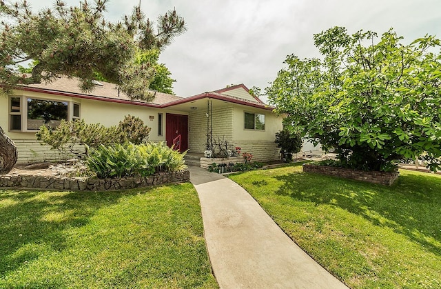 ranch-style house with stucco siding, a front lawn, brick siding, and stone siding