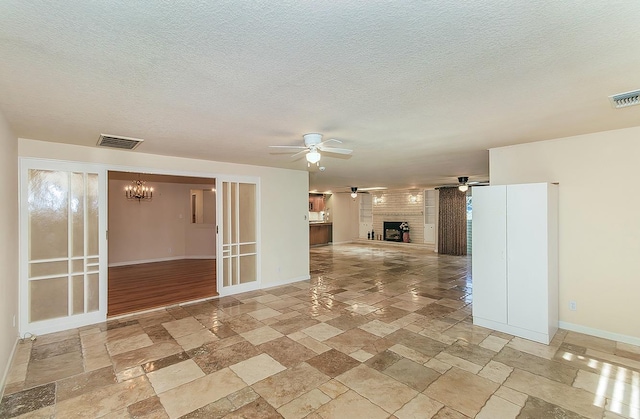 unfurnished living room featuring baseboards, stone tile flooring, visible vents, and ceiling fan with notable chandelier