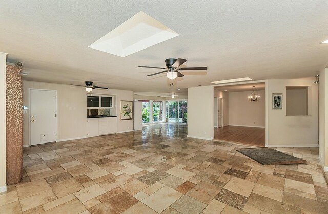 empty room with stone tile floors, baseboards, and ceiling fan with notable chandelier