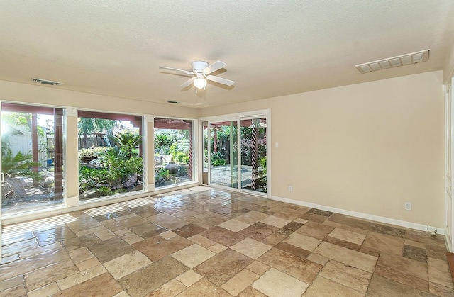 empty room featuring a ceiling fan, baseboards, stone tile floors, and visible vents
