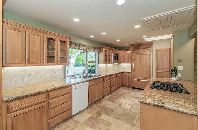 kitchen with backsplash, visible vents, a sink, light stone countertops, and built in appliances