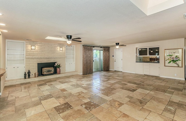 unfurnished living room featuring a ceiling fan, a textured ceiling, stone tile flooring, built in features, and a brick fireplace