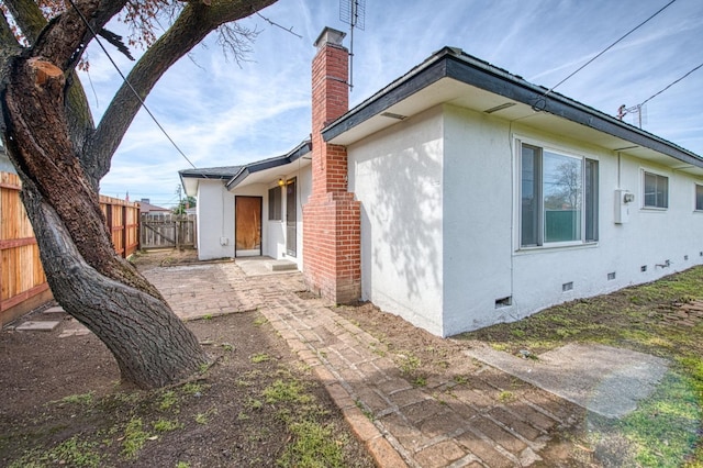 view of property exterior featuring fence, stucco siding, a chimney, a patio area, and crawl space