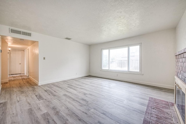 unfurnished living room featuring a textured ceiling, visible vents, and light wood-type flooring