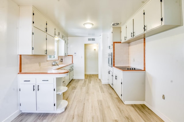 kitchen with decorative backsplash, light wood-style flooring, and oven