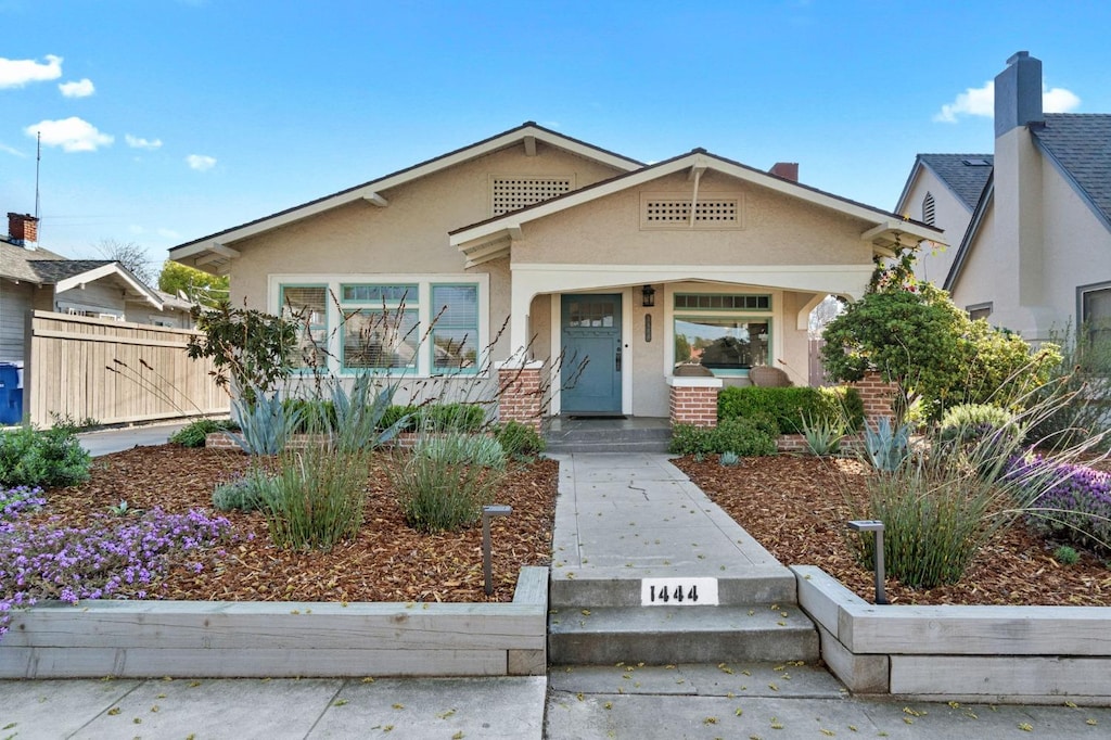 bungalow-style home with stucco siding and fence