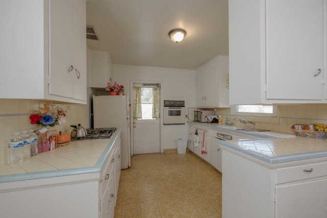 kitchen featuring plenty of natural light, white appliances, tile countertops, and white cabinetry