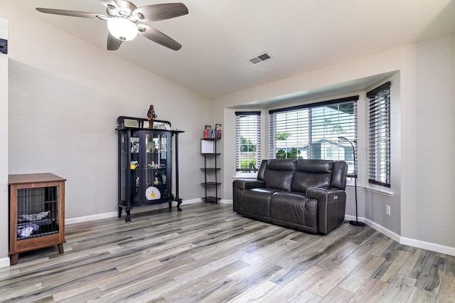 living area with visible vents, baseboards, a ceiling fan, light wood-style floors, and vaulted ceiling