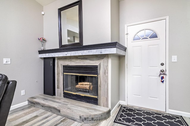 foyer entrance featuring baseboards, wood finished floors, and a tile fireplace