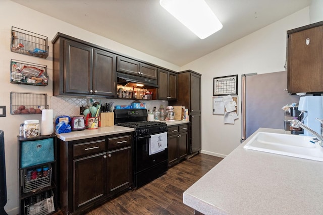 kitchen featuring dark brown cabinets, vaulted ceiling, under cabinet range hood, a sink, and black gas range