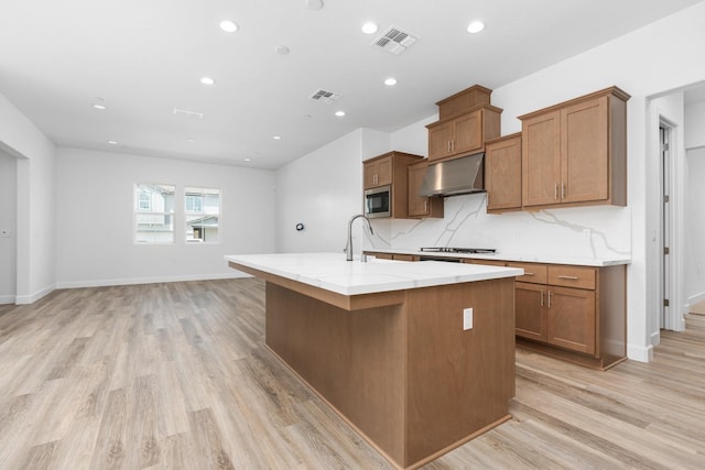 276 Huckleberry Ln S, Madera, CA 93636 - kitchen featuring an island with sink, stainless steel microwave, under cabinet range hood, and visible vents