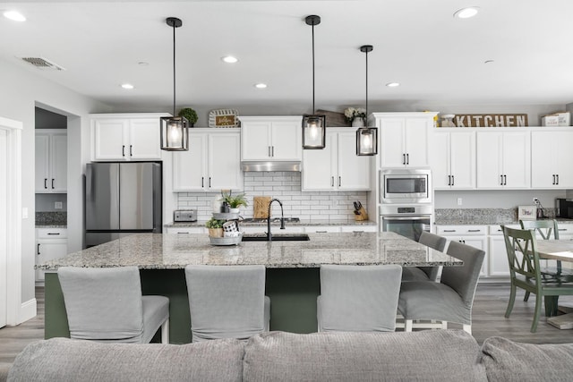 3887 N Condor Ct, Sanger, CA 93657 - kitchen featuring appliances with stainless steel finishes, white cabinetry, a kitchen breakfast bar, an island with sink, and light wood-style floors