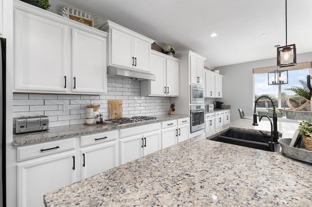 3887 N Condor Ct, Sanger, CA 93657 - kitchen featuring appliances with stainless steel finishes, white cabinets, tasteful backsplash, under cabinet range hood, and hanging light fixtures