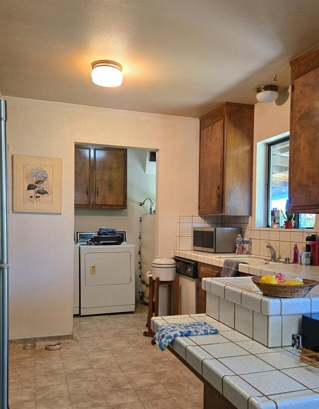 26174 Haley Way, Madera, CA 93638 - kitchen featuring tasteful backsplash, brown cabinetry, stainless steel microwave, independent washer and dryer, and tile countertops