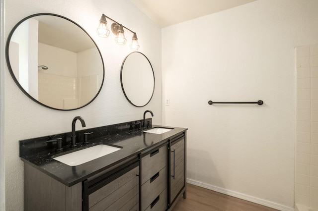 full bathroom with double vanity, a sink, baseboards, and wood finished floors