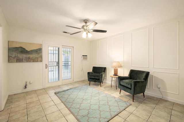 sitting room with visible vents, a ceiling fan, a decorative wall, and light tile patterned floors
