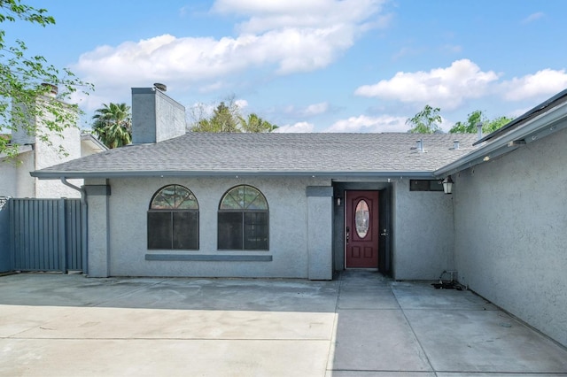 view of exterior entry with stucco siding, a shingled roof, a chimney, and a patio area