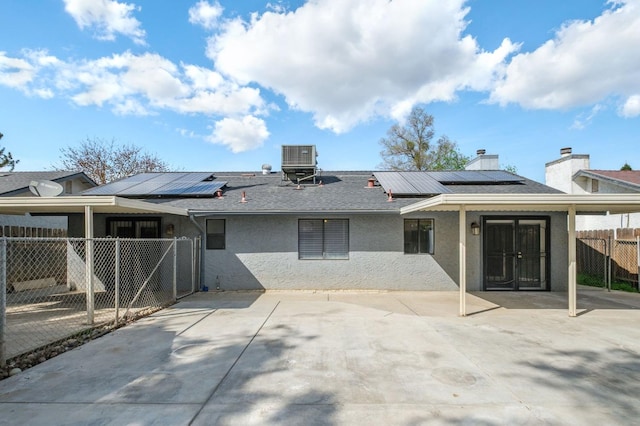 back of property featuring roof mounted solar panels, cooling unit, fence, and stucco siding