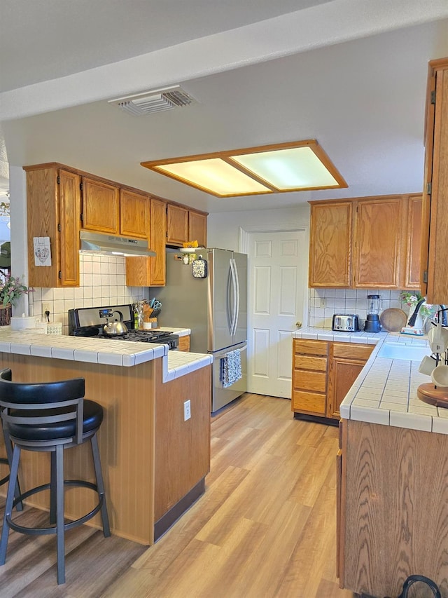 1295 E Athens Ave, Fresno, CA 93720 - kitchen featuring tile counters, under cabinet range hood, a peninsula, backsplash, and stainless steel appliances