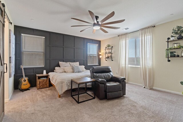carpeted bedroom with a decorative wall, baseboards, a ceiling fan, and visible vents