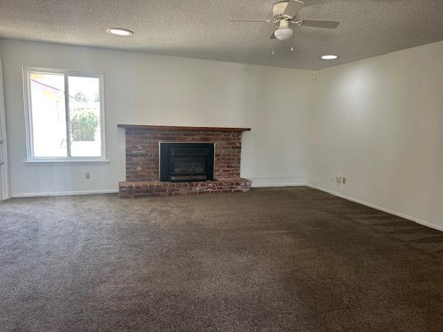309 Circle Dr, Chowchilla, CA 93610 - unfurnished living room featuring baseboards, a textured ceiling, a ceiling fan, a brick fireplace, and carpet