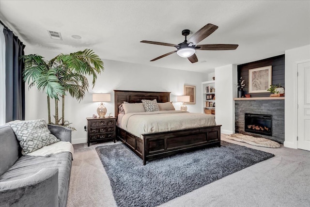 carpeted bedroom featuring baseboards, ceiling fan, visible vents, and a stone fireplace