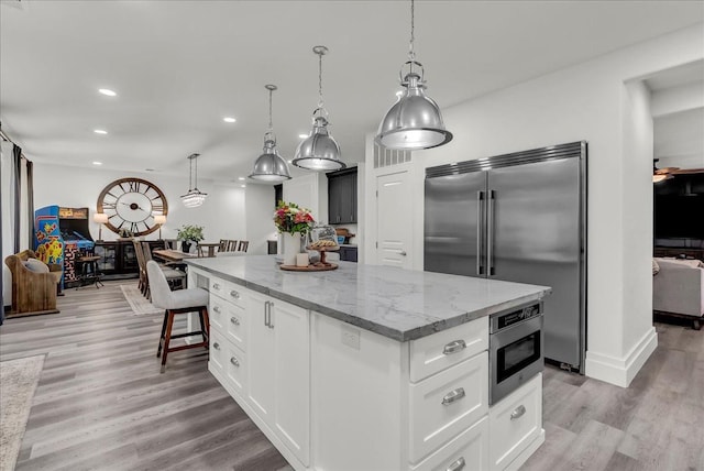 kitchen with light stone counters, light wood finished floors, built in appliances, a center island, and recessed lighting