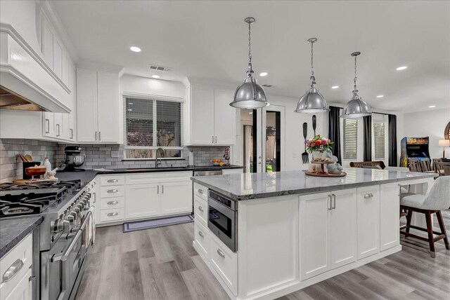kitchen with stainless steel appliances, a sink, a kitchen island, visible vents, and custom exhaust hood