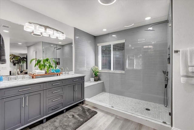 full bath with a sink, a shower stall, wood finished floors, visible vents, and double vanity