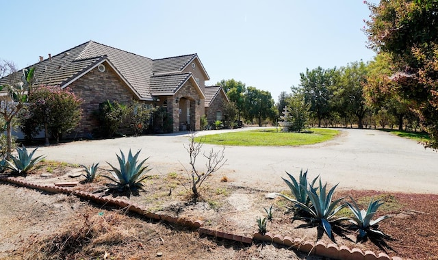 view of side of property with stone siding, a tiled roof, and a lawn