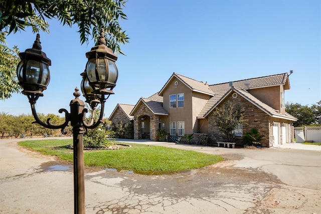 view of front facade featuring stucco siding, fence, stone siding, a tiled roof, and driveway