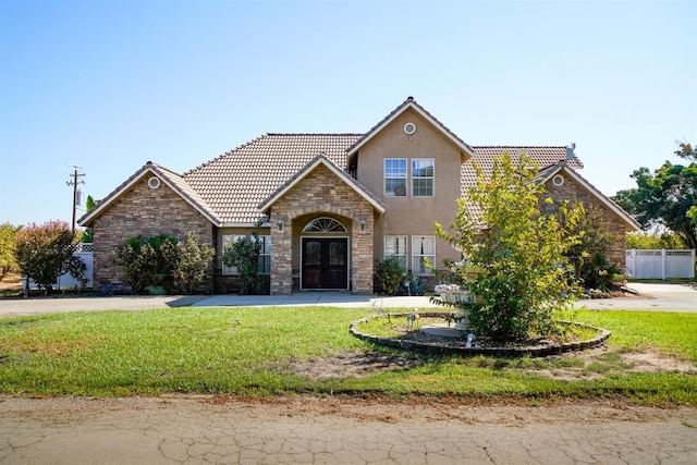 traditional-style home featuring a tile roof, a front yard, stone siding, stucco siding, and fence