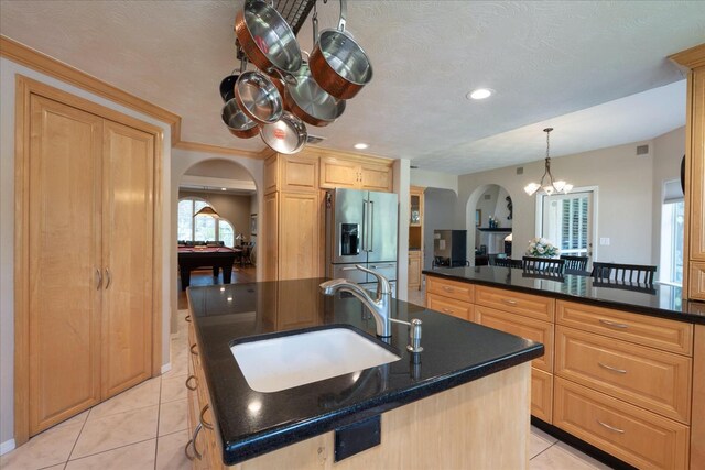 kitchen with a sink, an island with sink, stainless steel fridge with ice dispenser, arched walkways, and light tile patterned floors