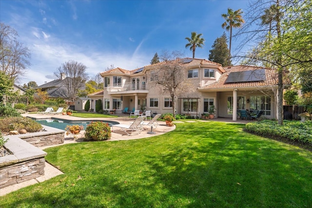 rear view of property with a lawn, a patio, solar panels, and a balcony